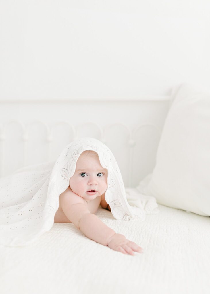 Six-month-old baby lying on a white bed during a milestone photography session in Jupiter, Florida