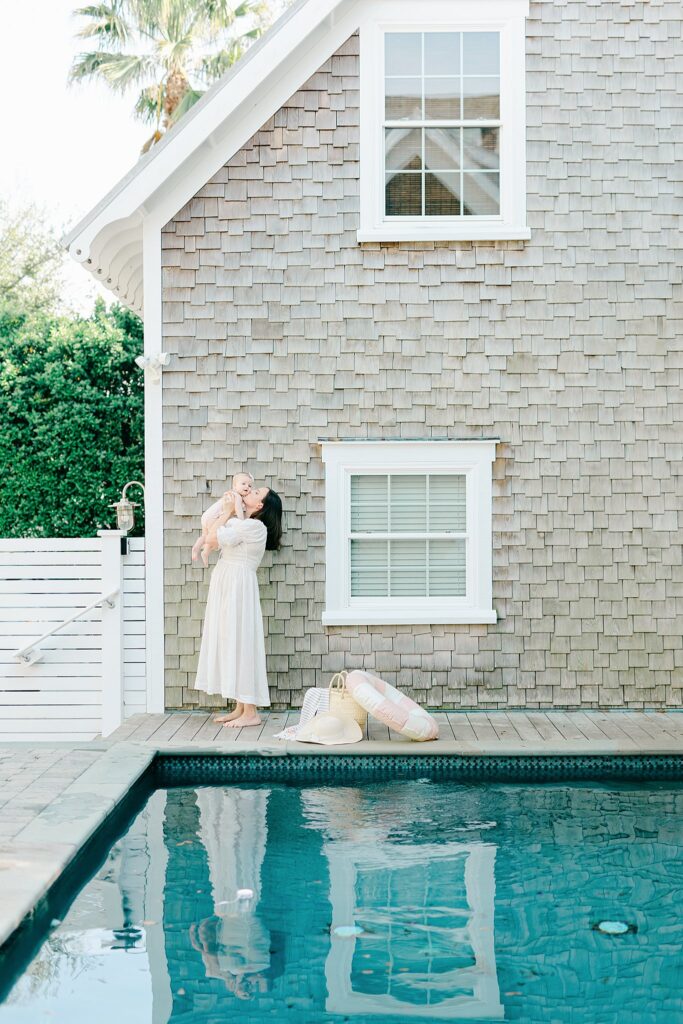 Timeless lifestyle photo of a mom holding her baby near a coastal cottage, taken by a Jupiter FL family photographer specializing in meaningful, stress-free portraits.
