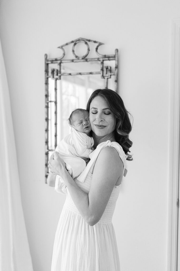 Mother gently cradling her newborn near a mirror during an in-home session in Jupiter — captured with a full-service newborn photography experience.