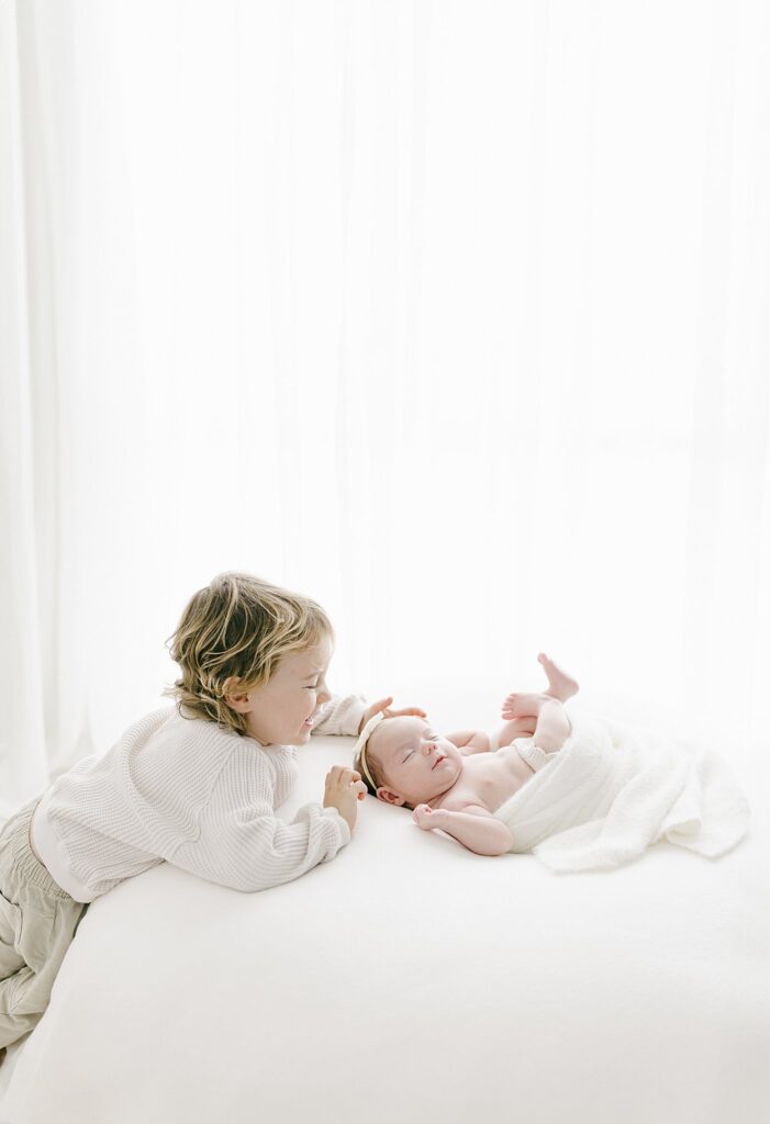 Tender moment between toddler and newborn sibling on soft white bedding — part of a relaxed newborn and family photo session in Stuart, FL.