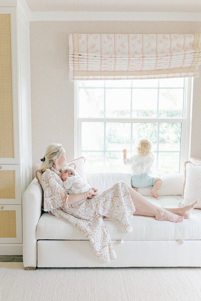 Candid lifestyle portrait of mom nursing newborn while toddler looks out window — part of a relaxed, full-service newborn session in Tequesta.